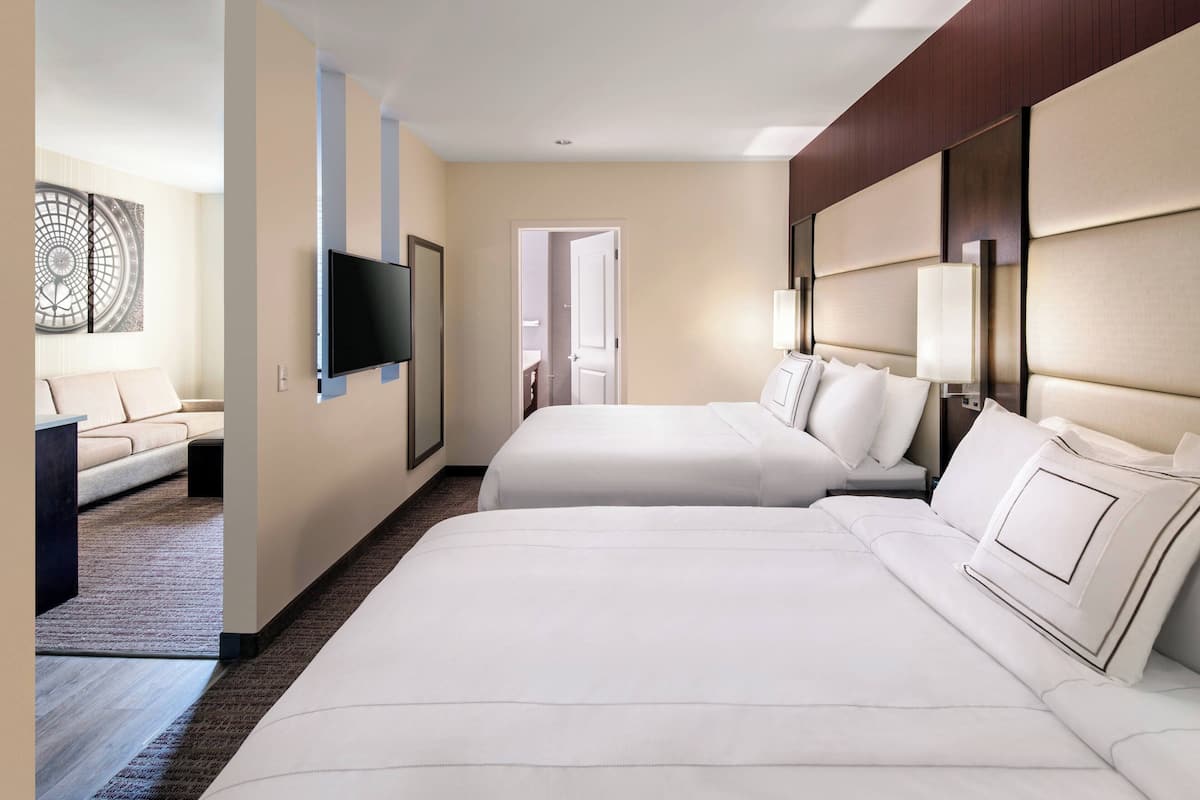 A hotel room with two beds, a TV mounted on the wall, and a door leading to another room.