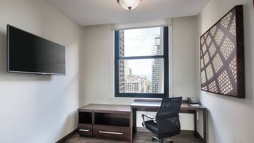 A modern office space with a large window, a desk, a chair, and a flat-screen TV mounted on the wall.