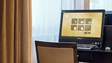 A hotel room with a desktop computer, a wooden chair, and a window with curtains.