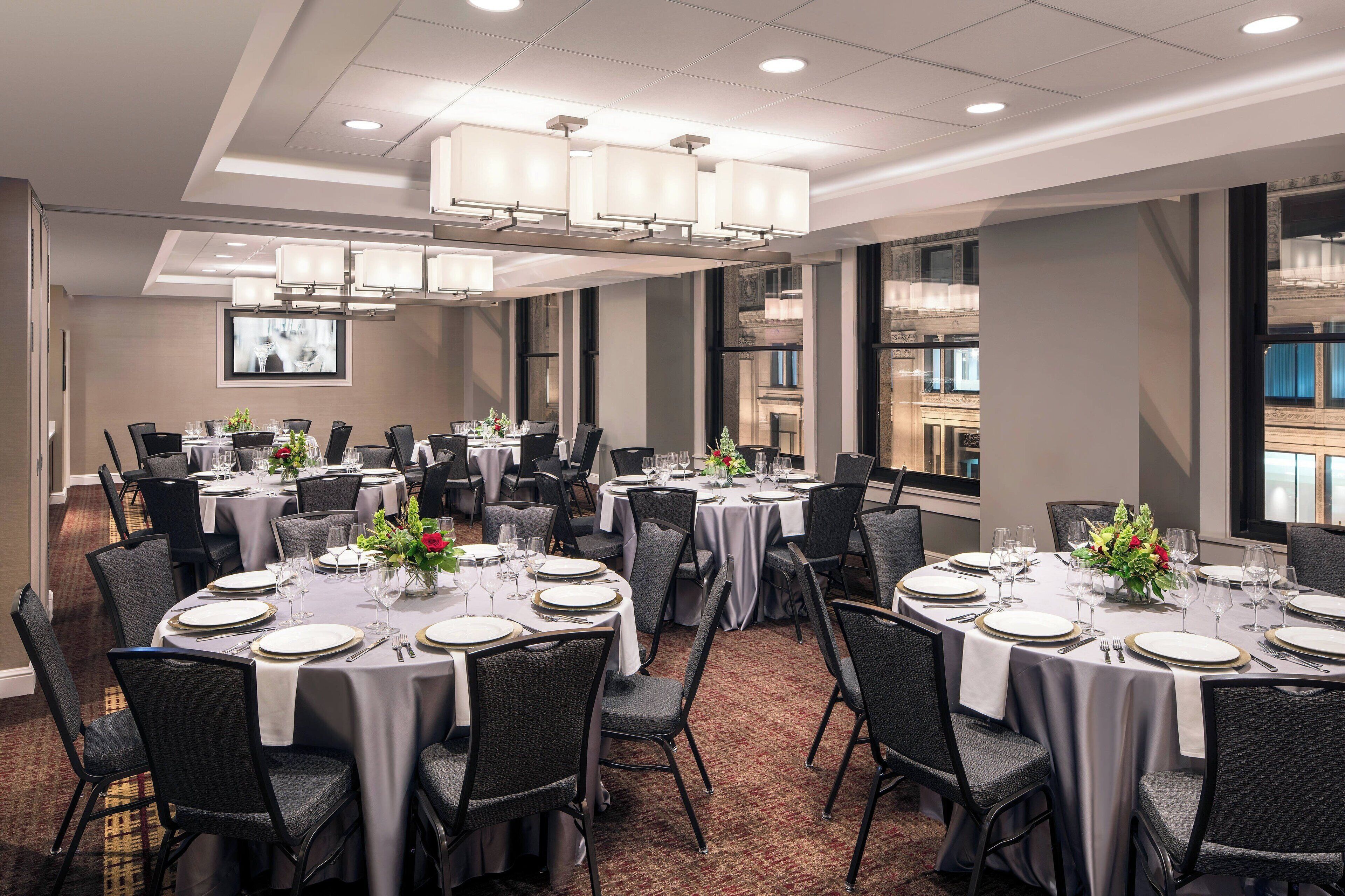A conference room with round tables, black chairs, and white tablecloths.