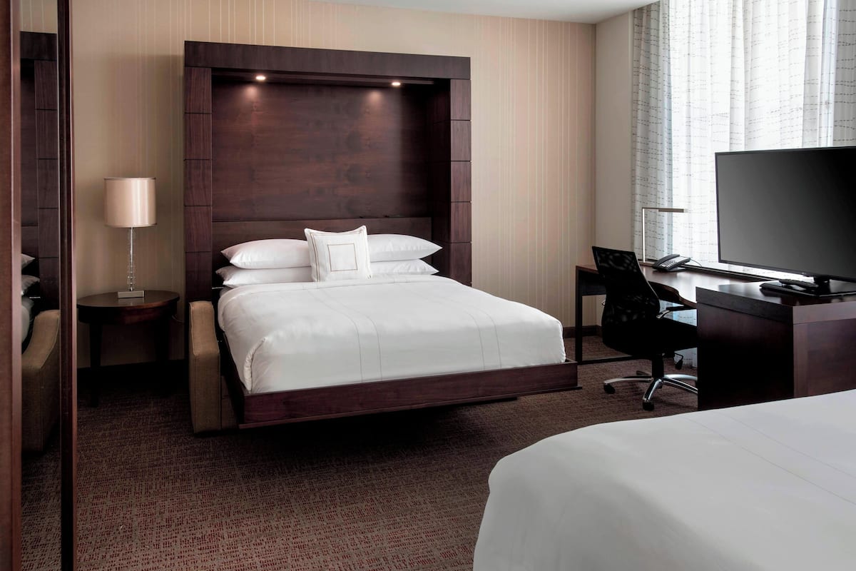 A hotel room with a large bed, a desk with a computer, a TV, and a lamp.
