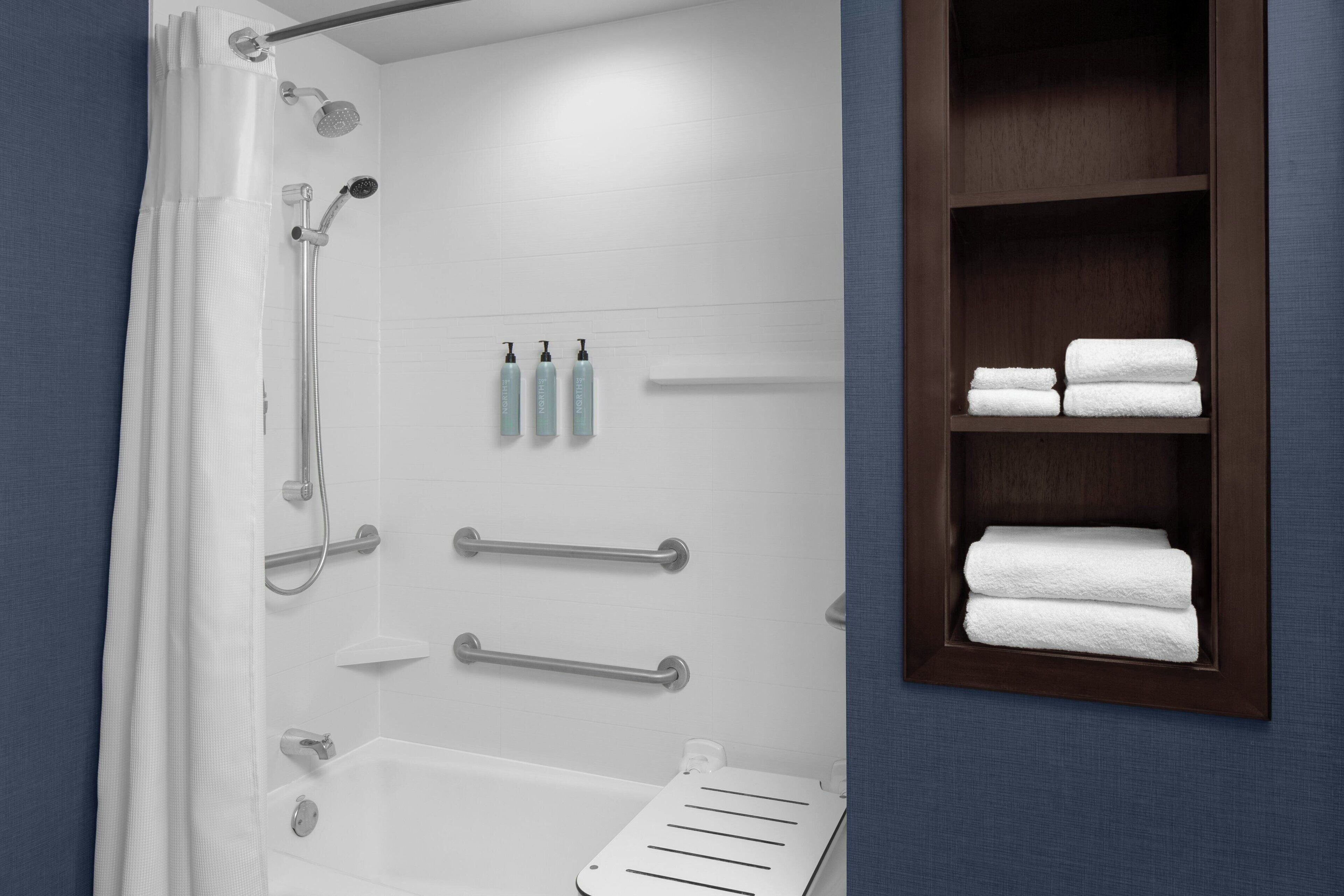 Une salle de bain moderne équipée d’une douche, de barres d’appui, d’un porte-serviettes et d’une étagère où sont pliés les serviettes.