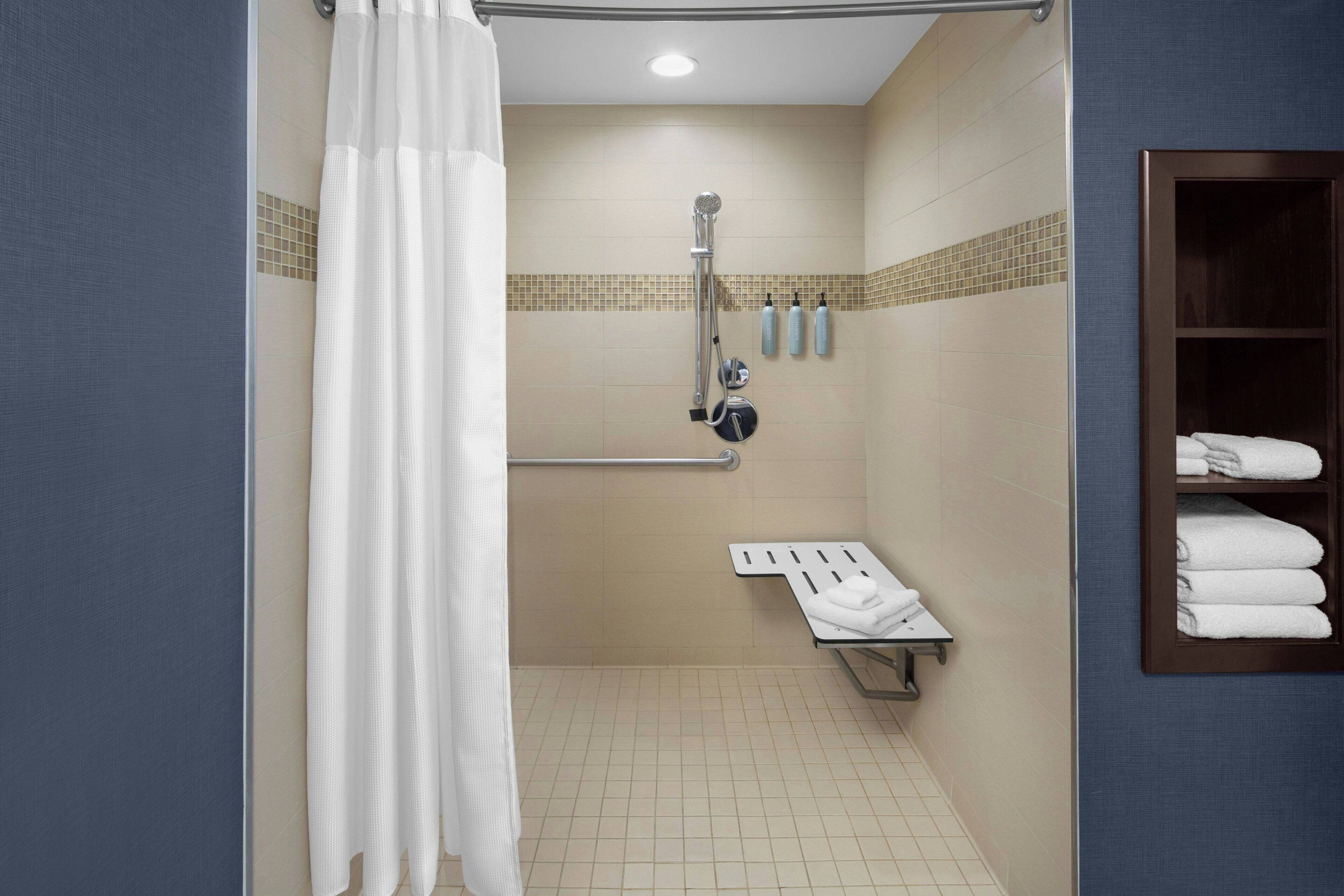 A shower area with a grab bar, a towel rack, and a shelf with towels.
