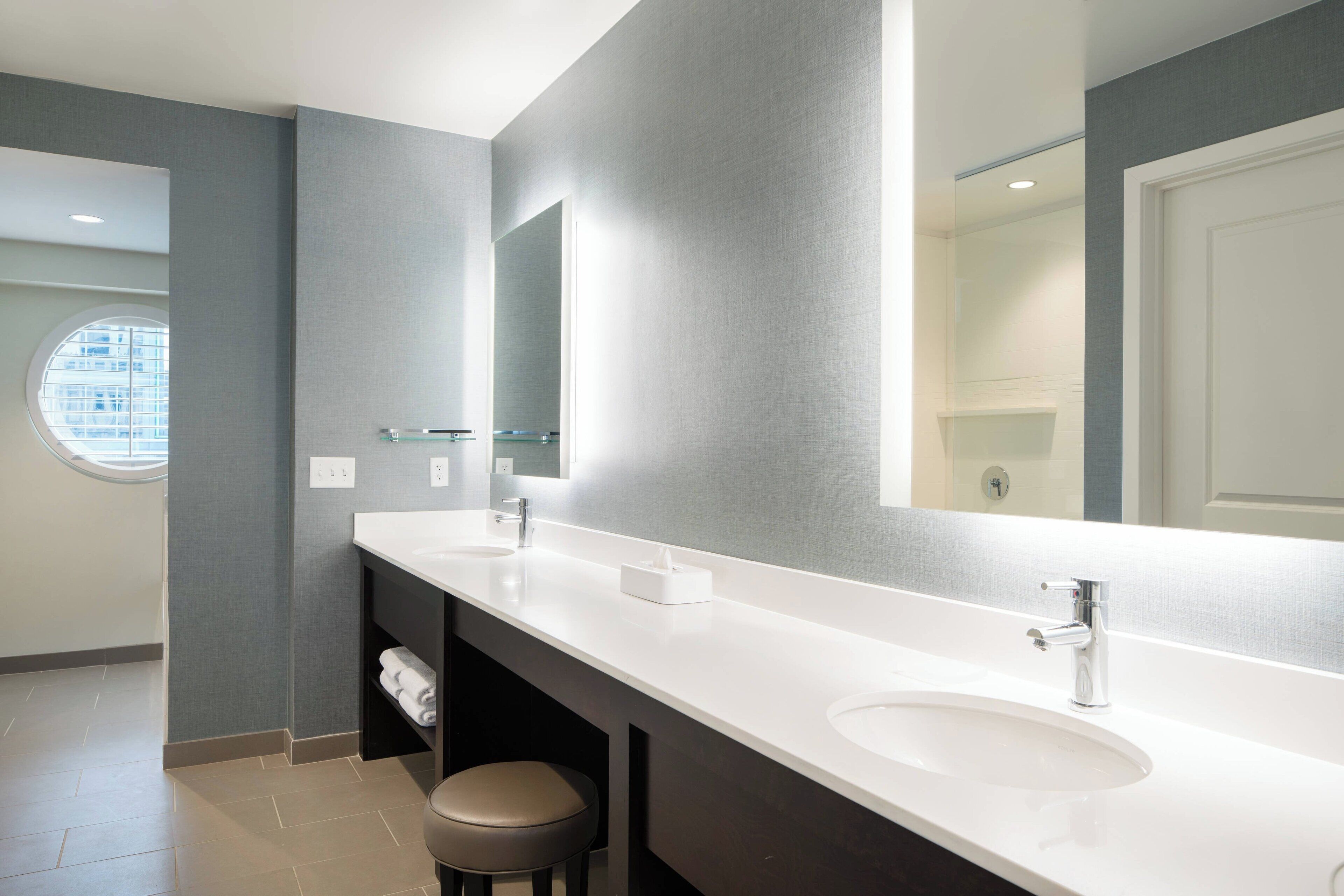 A modern bathroom with two sinks, a large mirror, and a round window.