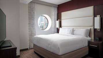A hotel room with a large bed, a round window, a nightstand, and a wall-mounted TV.