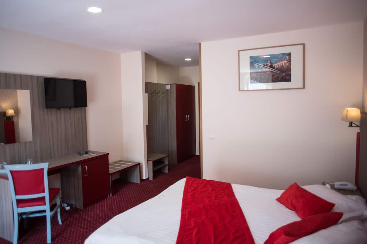 A hotel room with a bed, a desk, a chair, a television, and a wardrobe.