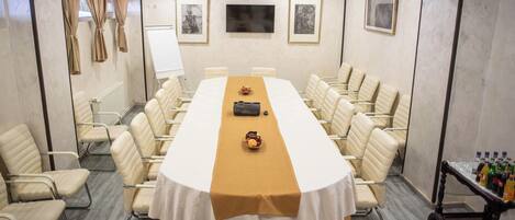 A conference room with a long table, beige chairs, a whiteboard, framed pictures, and a beverage cart.