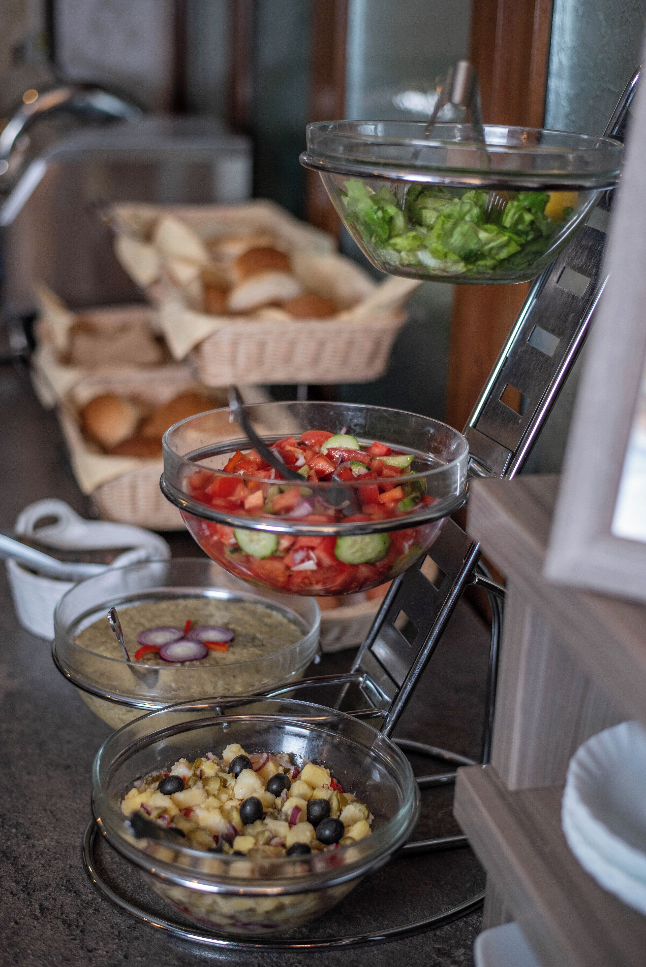 Un bufé con diversas opciones de comida, incluyendo una ensalada, un cuenco de aceitunas y un recipiente con pan.