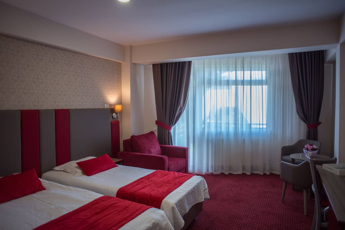 A hotel room with two beds, a desk, a chair, and a large window with curtains.