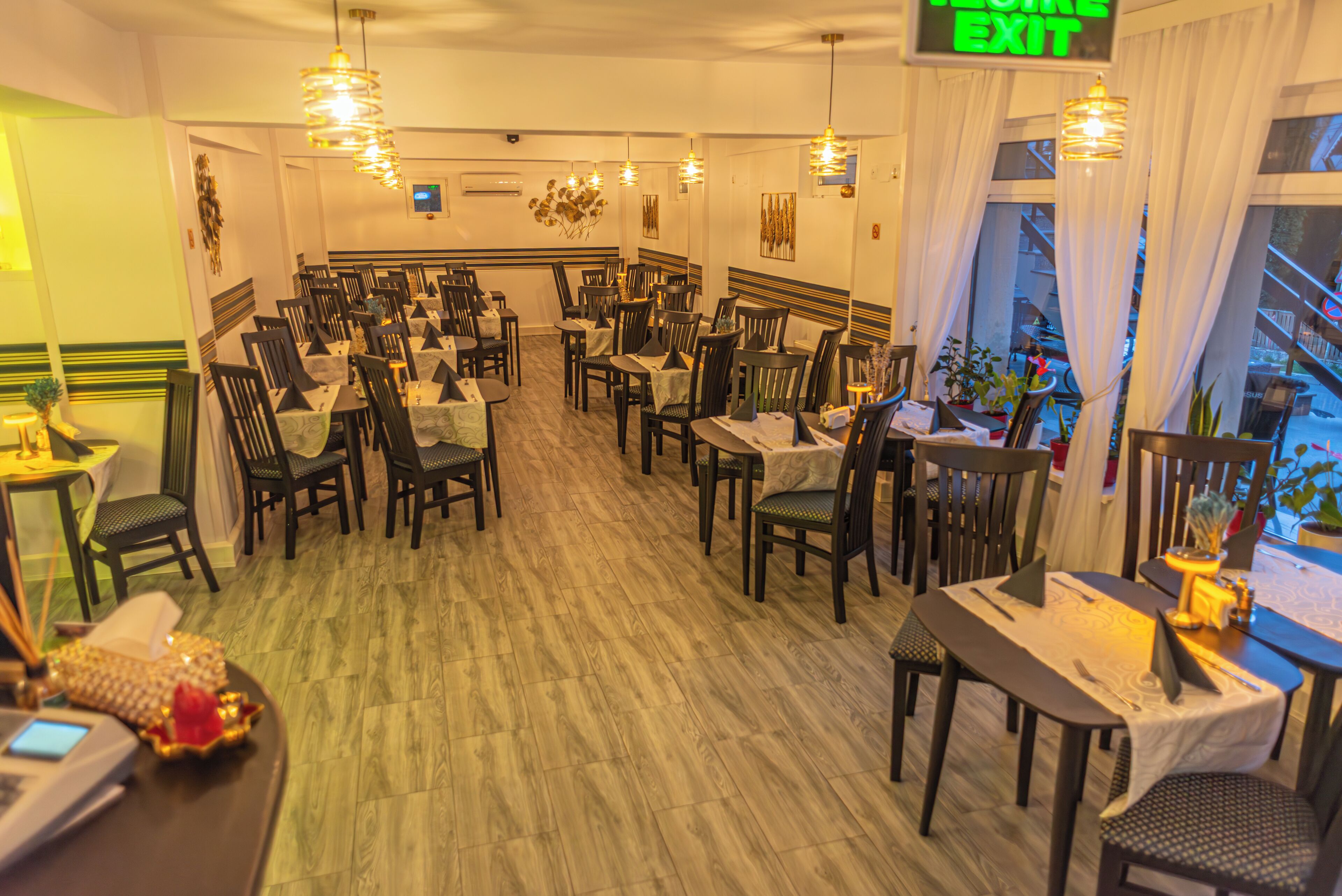 A restaurant with multiple tables and chairs, a sign indicating the exit, and a view of the outside through large windows.