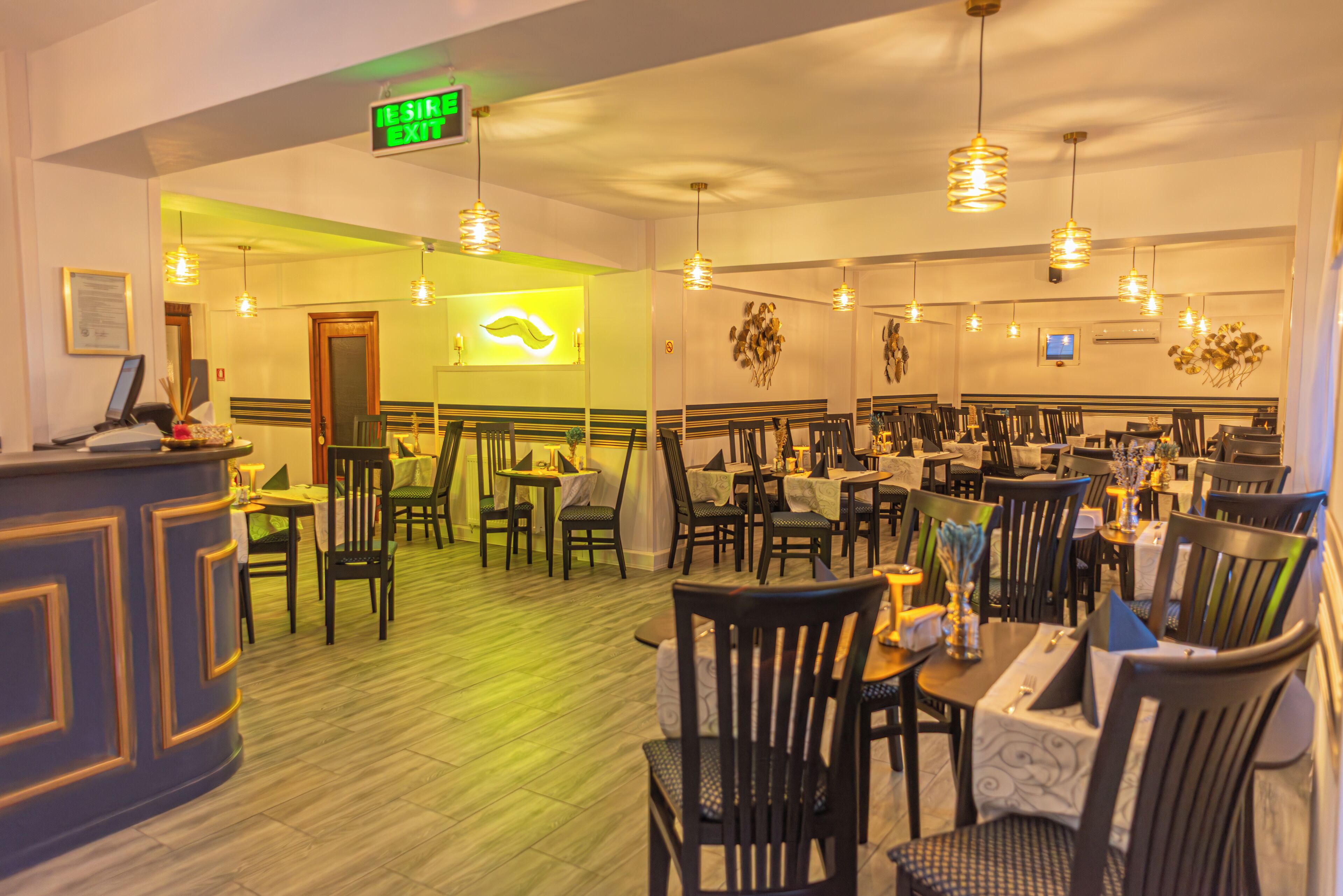 A restaurant with a reception area, multiple dining tables, and chairs. There is a sign indicating the exit.
