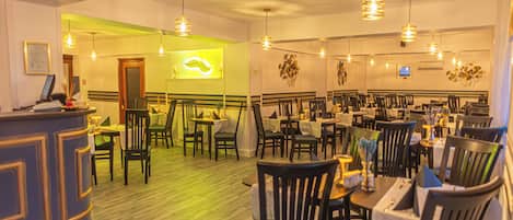 A restaurant with a reception area, multiple dining tables, and chairs. There is a sign indicating the exit.