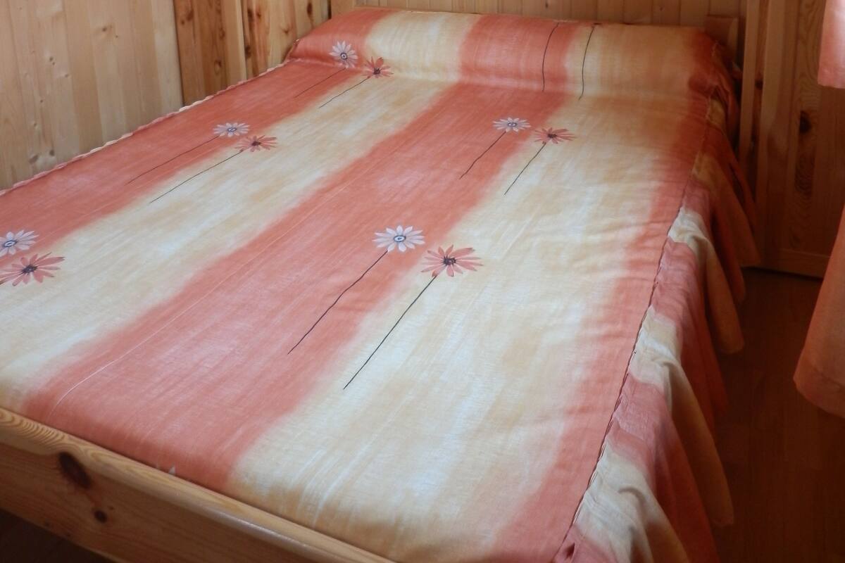 Una habitación de cabaña de madera con una cama individual, un estante de madera sobre la cama y una pequeña ventana.