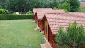 A row of wooden cabins with pitched roofs, set in a grassy area with trees in the background. - Camping Lluçanés (Olost)