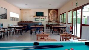 A classroom with tables and chairs, a pool table, and a television on the wall. - Camping Lluçanés (Olost)