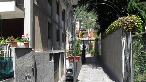 A narrow urban street with buildings on either side, a parked car, and potted plants. - Hotel Ristorante Al Caminetto (Aosta)