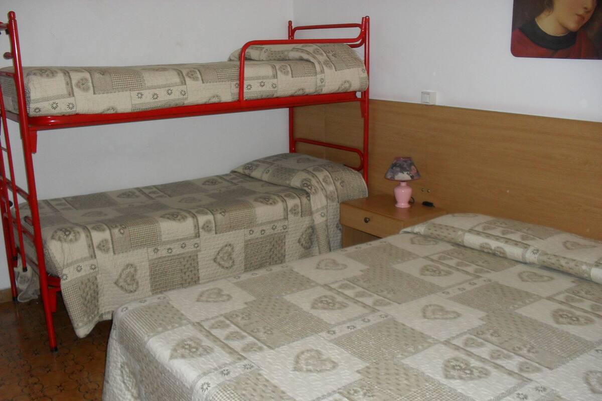 A bunk bed room with a wooden headboard, a small bedside table with a lamp, and a patterned bedspread.