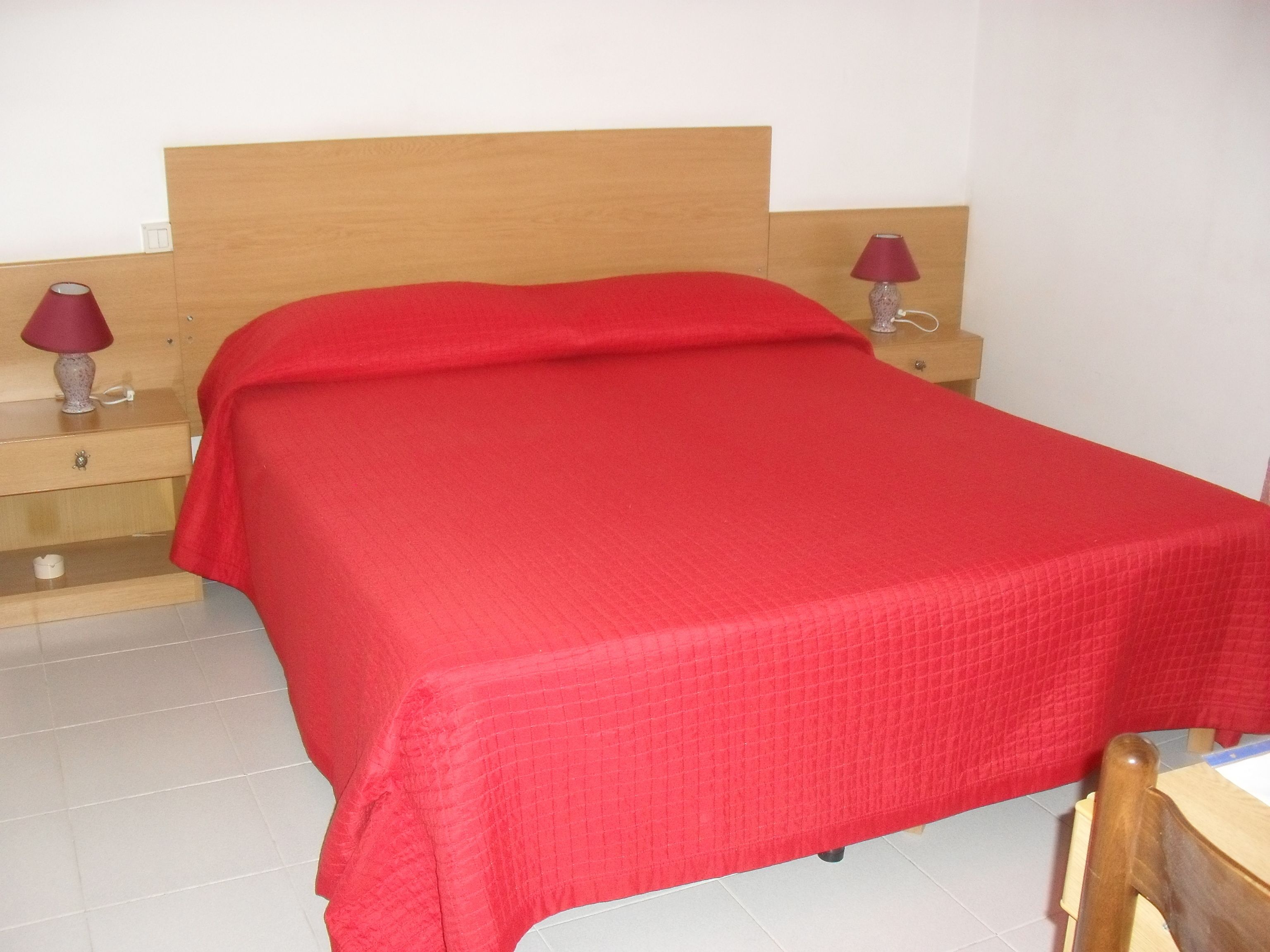 A bed with a wooden headboard, two bedside tables with lamps, and a red bedspread.