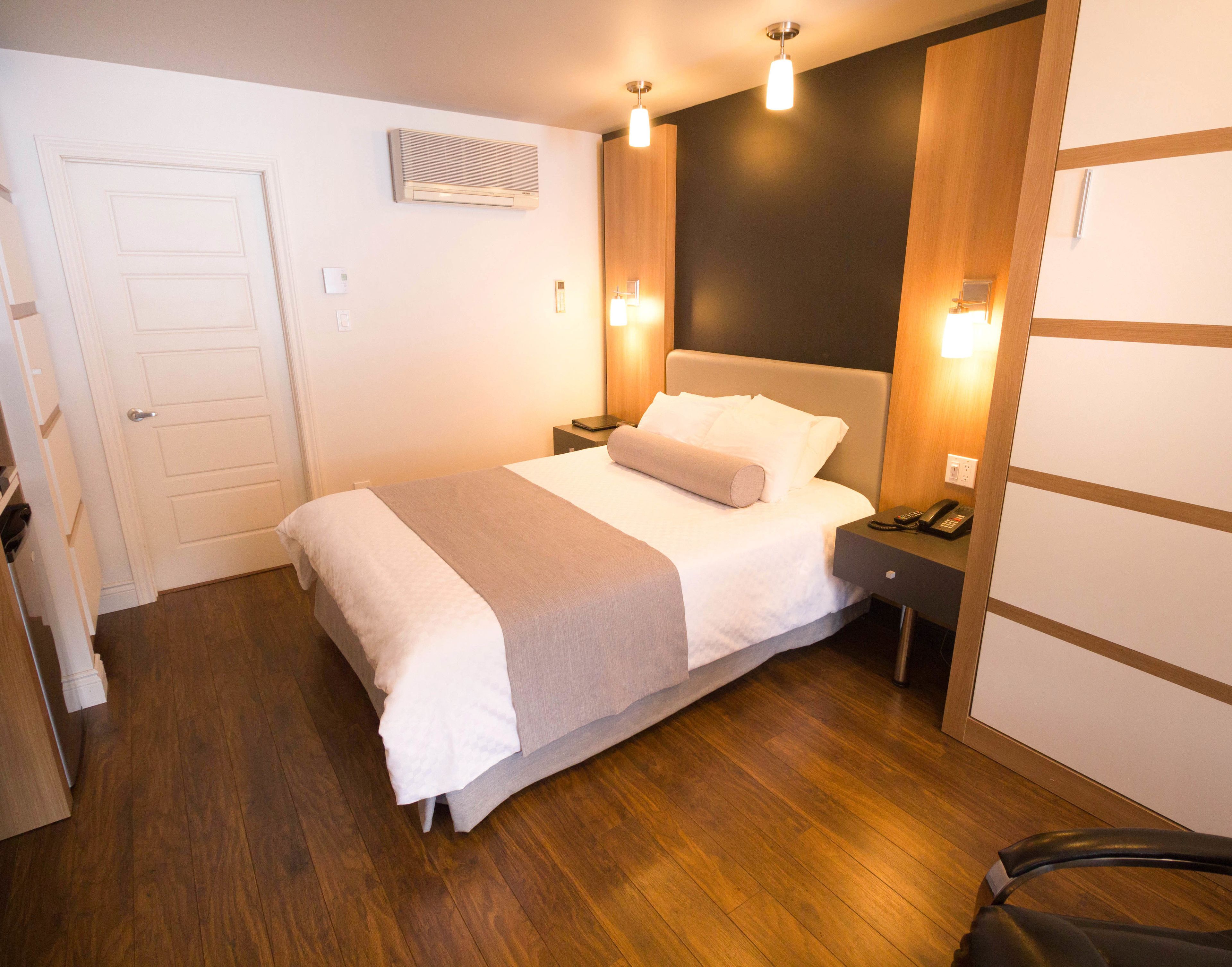 Una habitación de hotel con cama, mesitas de noche, teléfono y aire acondicionado instalado en la pared.