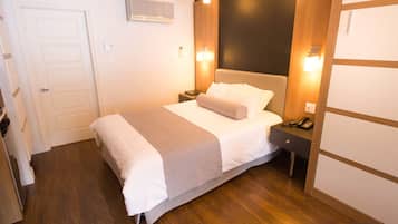 Una habitación de hotel con cama, mesitas de noche, teléfono y aire acondicionado instalado en la pared.