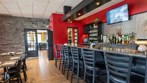 A bar area with a long counter, multiple bar stools, and a television mounted on the wall.