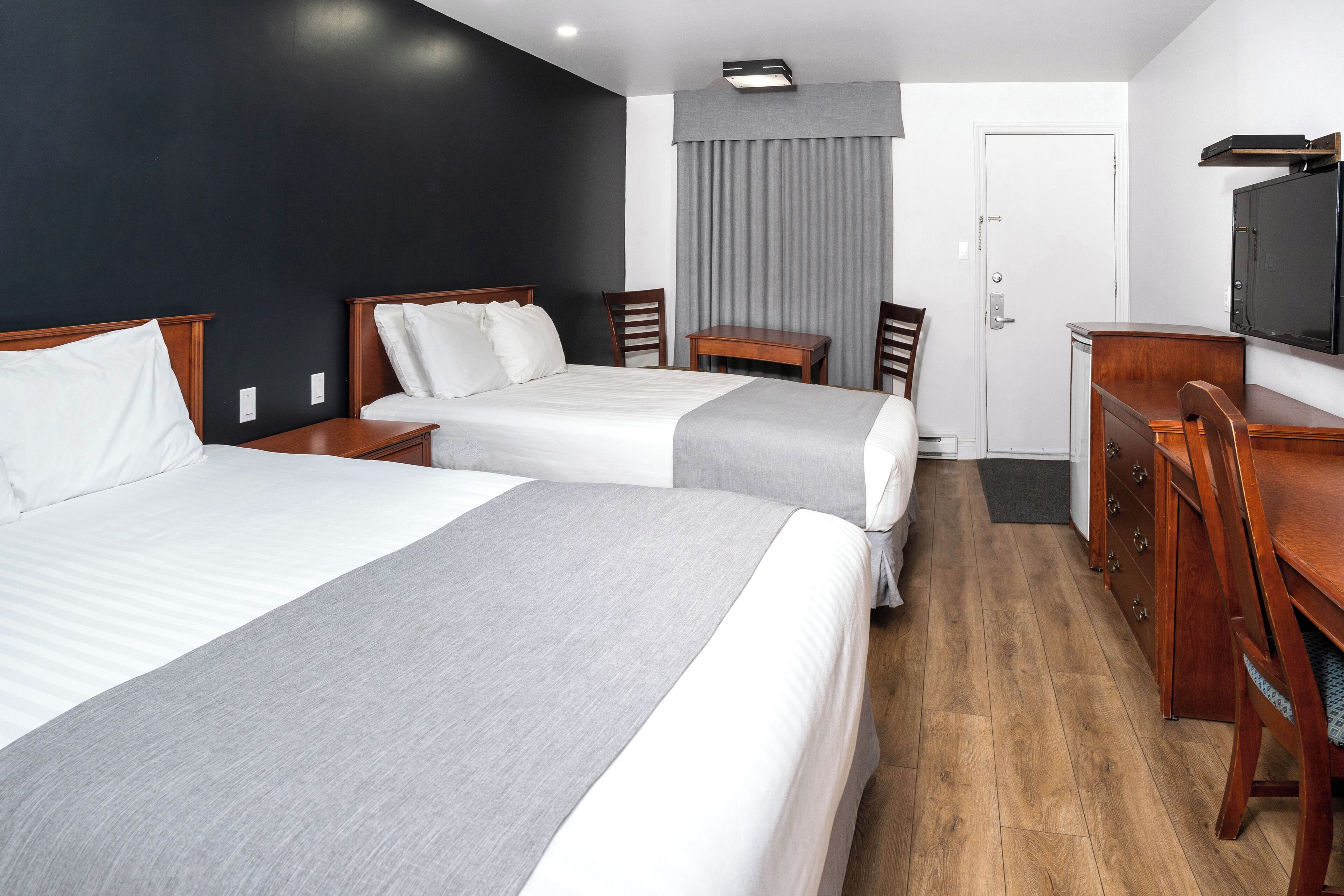 Habitación de hotel con dos camas, un escritorio, una silla, un televisor y una puerta.