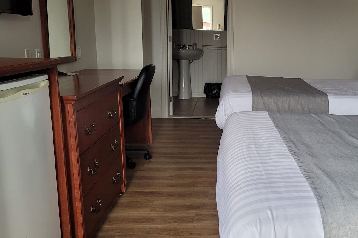 A hotel room with two beds, a wooden dresser, a desk, and a bathroom visible through an open door.