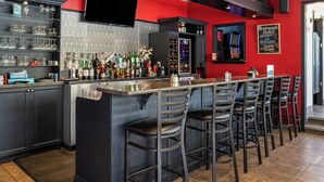 A bar area with a long counter, multiple stools, and a variety of bottles and glasses on shelves.