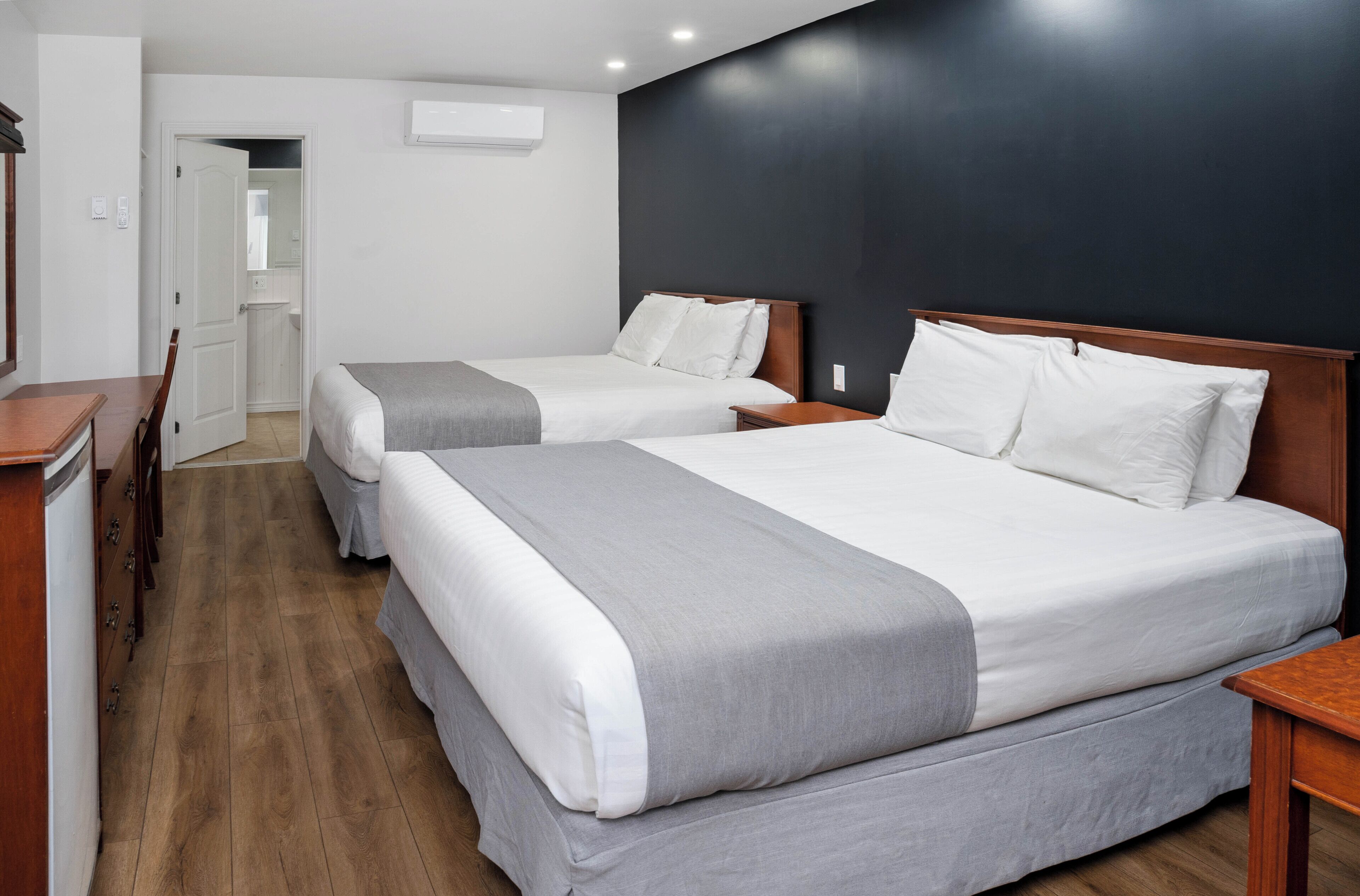 Habitación de hotel con dos camas, pisos de madera, una pared de acento oscura y una puerta blanca que da al baño.
