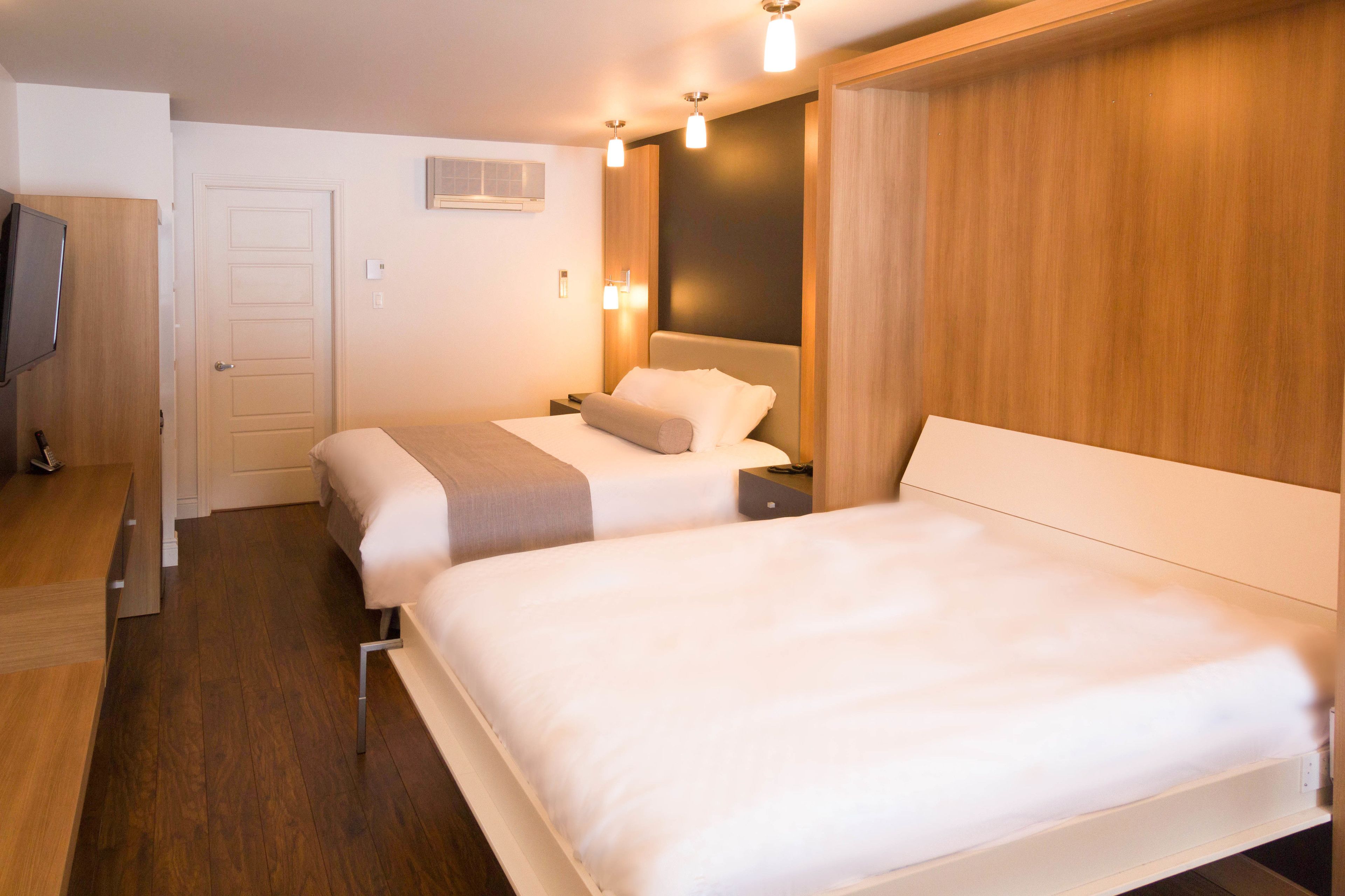 A hotel room with two beds, a wooden wardrobe, a flat-screen TV, and a wall-mounted air conditioner.
