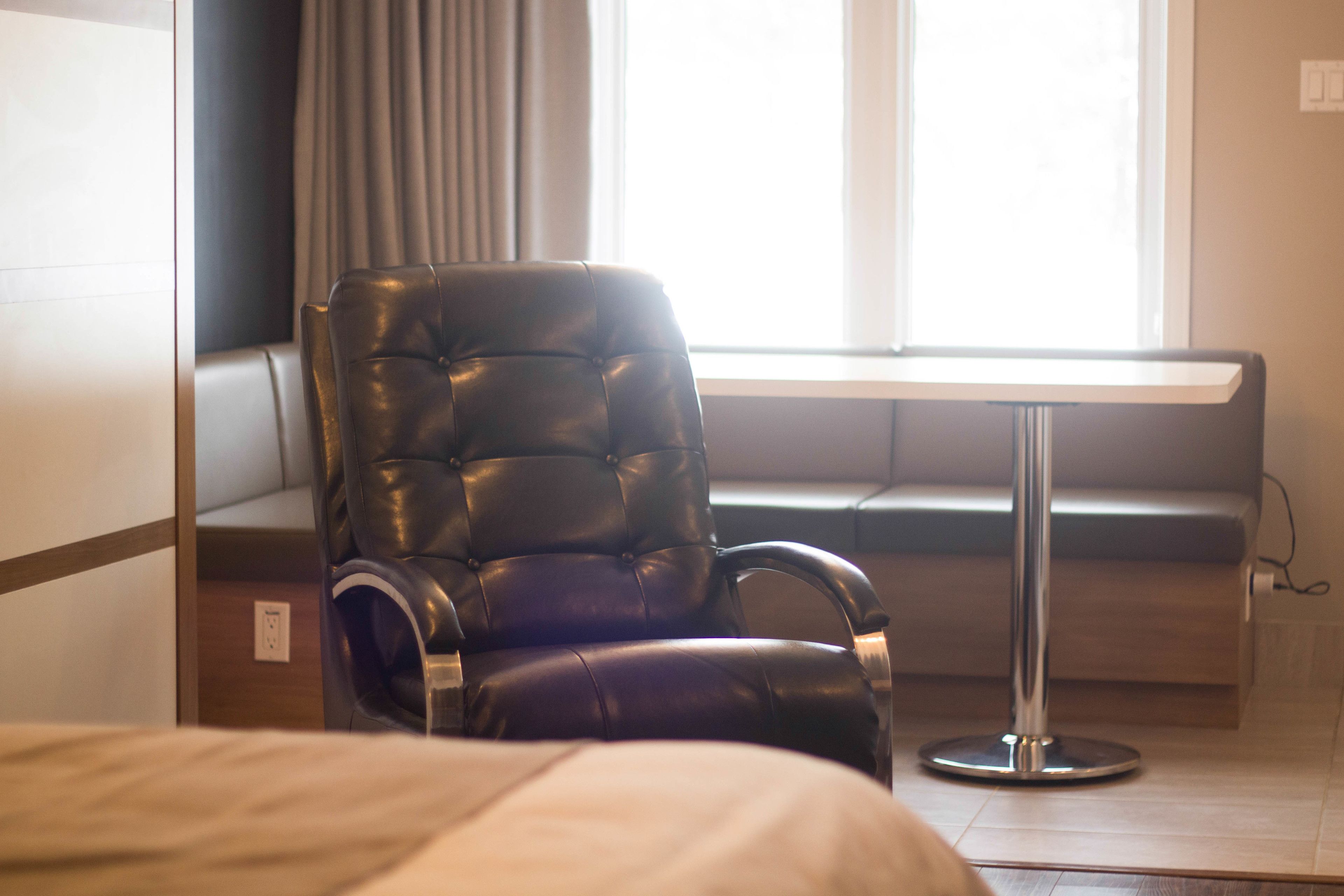 Ein modernes Hotelzimmer mit Ledersessel, einer Holzbank und einem kleinen Tisch.