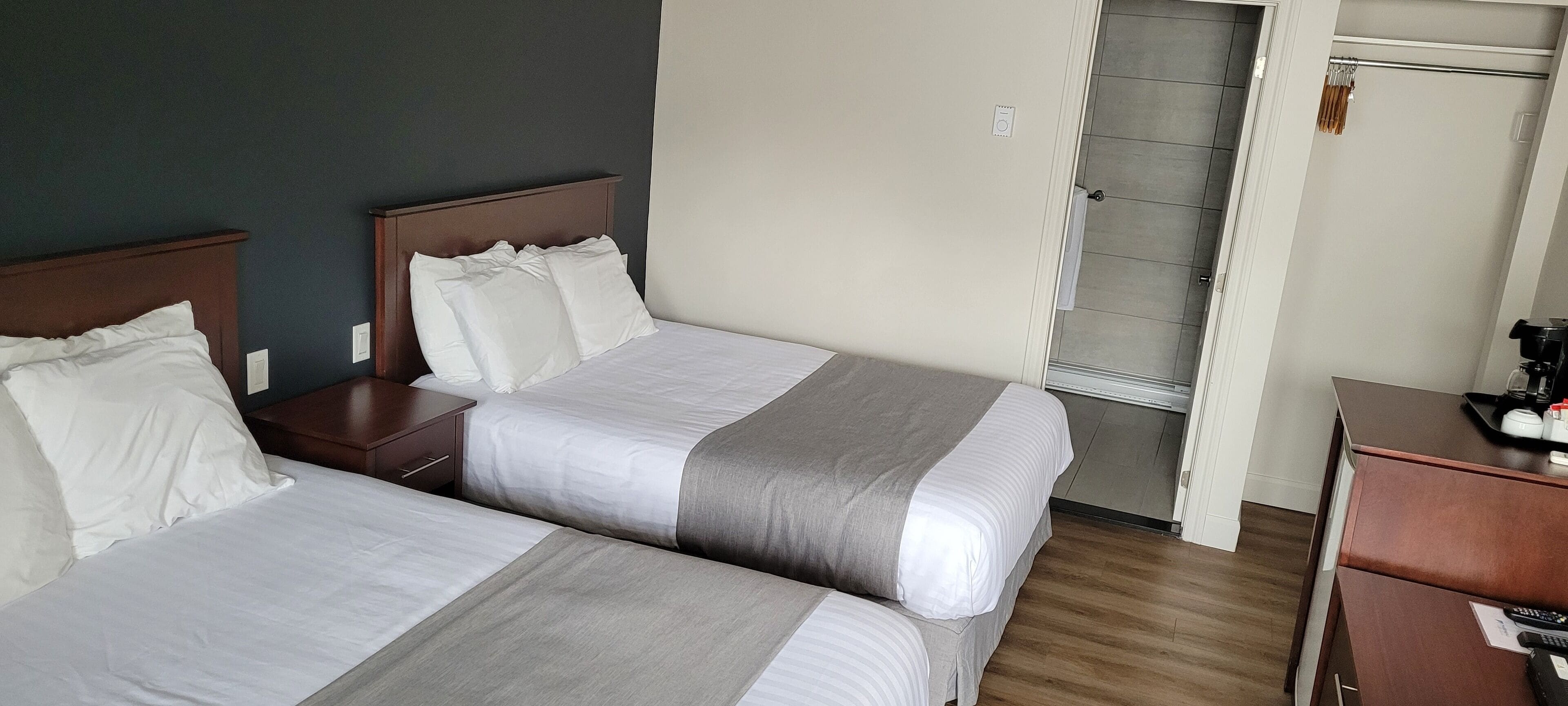 A hotel room with two beds, a wooden nightstand, a desk with a telephone, and a closet with a sliding door.