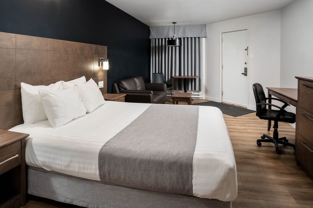 A hotel room with a large bed, a desk, a chair, a wardrobe, and a lamp.