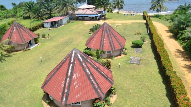 Un complexe hôtelier comprenant trois bâtiments de style bungalow, un bâtiment principal avec un toit bleu et une vue sur la plage.
