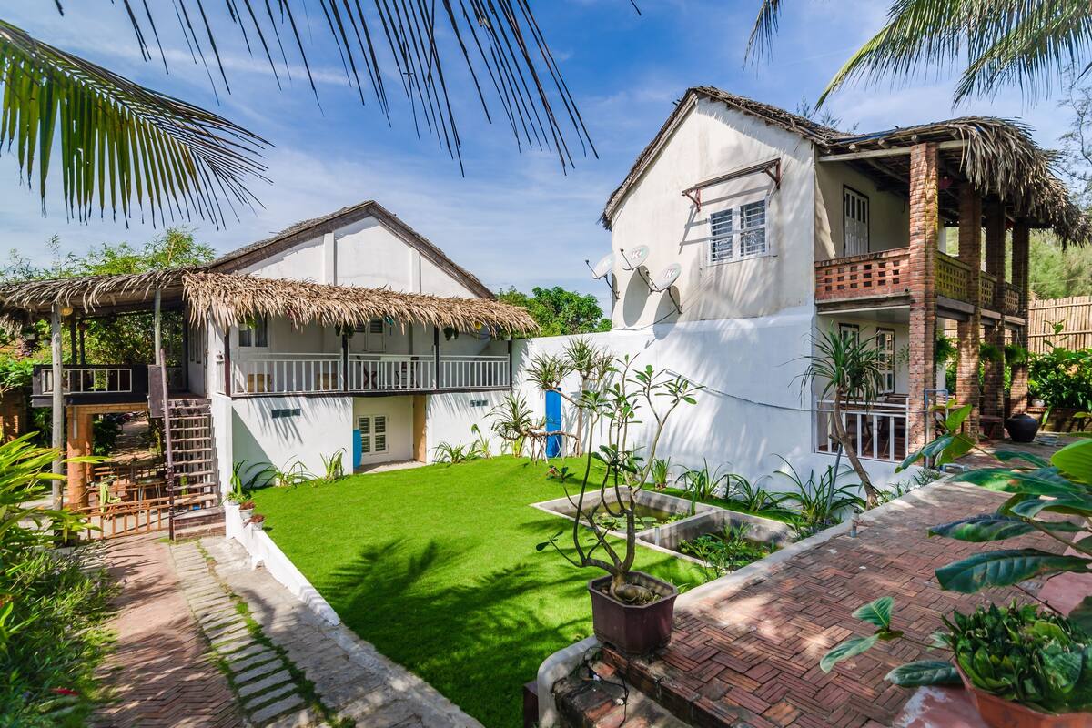A two-story house with a thatched roof, a small garden, and a paved pathway.