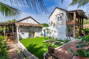 A two-story house with a thatched roof, a small garden, and a paved pathway. - Tan Thanh Garden Homestay (Da Nang)