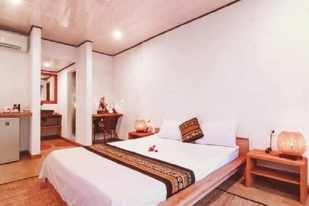 A hotel room with a bed, bedside table, lamp, and a desk with a chair.