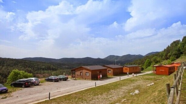 A rural setting with a row of wooden cabins, a gravel road, and a mountainous backdrop. - Camping Campalans (Borreda)