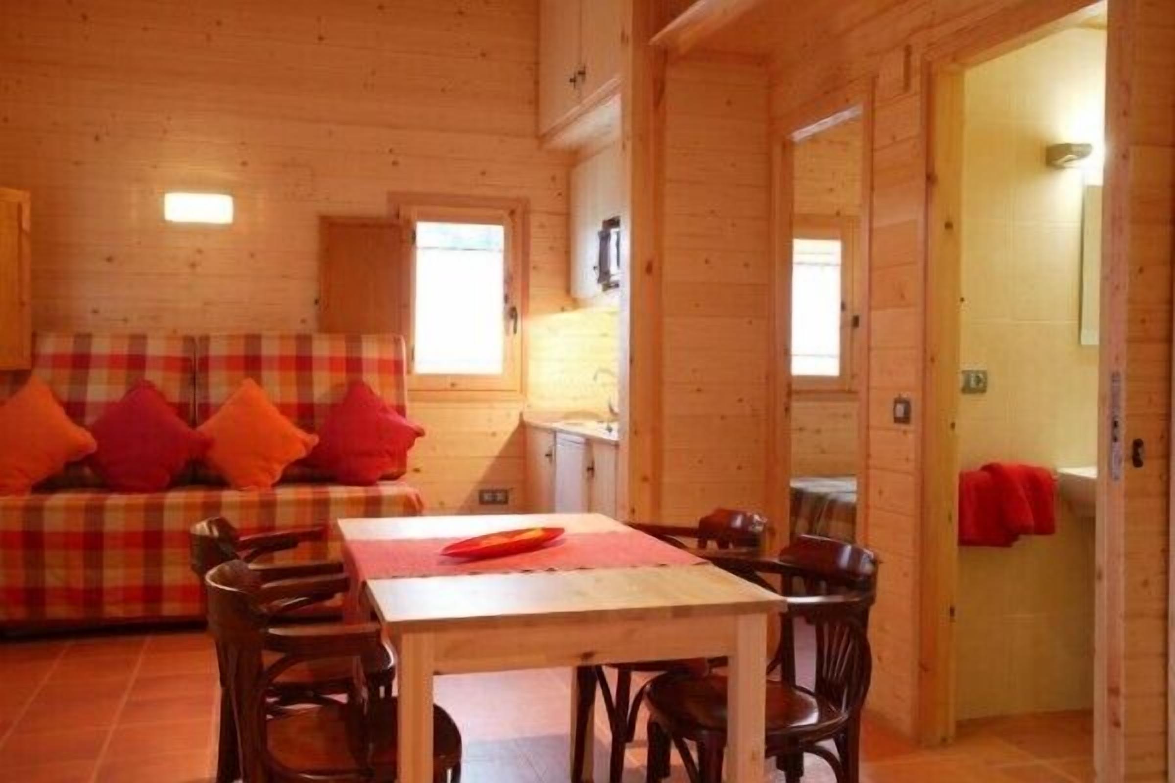 A cozy wooden cabin interior with a plaid sofa, a dining table, and chairs.