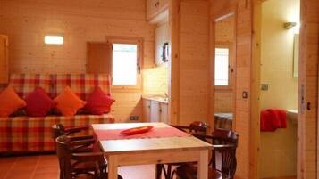 A cozy wooden cabin interior with a plaid sofa, a dining table, and chairs.