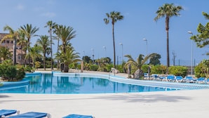Una piscina con agua azul, rodeada de palmeras y sillas de descanso azules.