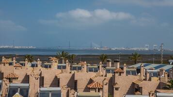 A coastal hotel with multiple rooms featuring solar panels and a view of the sea and a bridge in the distance.