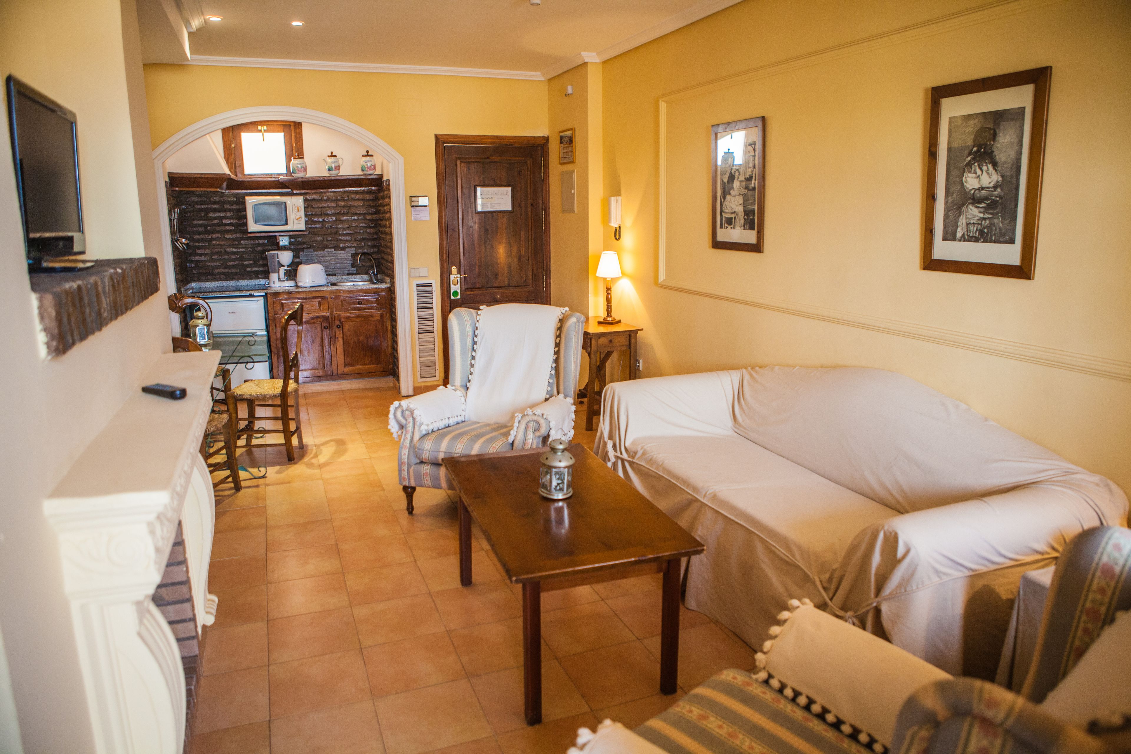 Un salon comprenant un canapé, un fauteuil et une petite table. Il y a également un coin cuisine avec un four à micro-ondes et une porte.