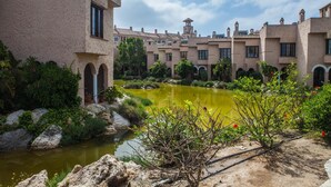 Un patio con un estanque, rodeado de edificios con ventanas de arco y una torre.