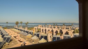 Vista costera de un resort con varias cabañas, palmeras y una vista despejada del mar y un puente distante.