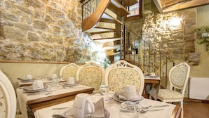 Un comedor con pared de piedra, una escalera en espiral y sillones tapizados con motivos florales.