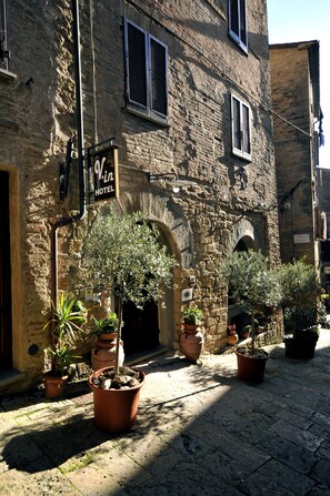 A stone building with a sign reading "Vin Hotel." There are potted plants in front of the entrance. - Hotel Volterra In Superior (Volterra)