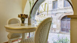 Un comedor con una mesa redonda y sillas, un florero con flores, y vista a un edificio de piedra a través de un arco.
