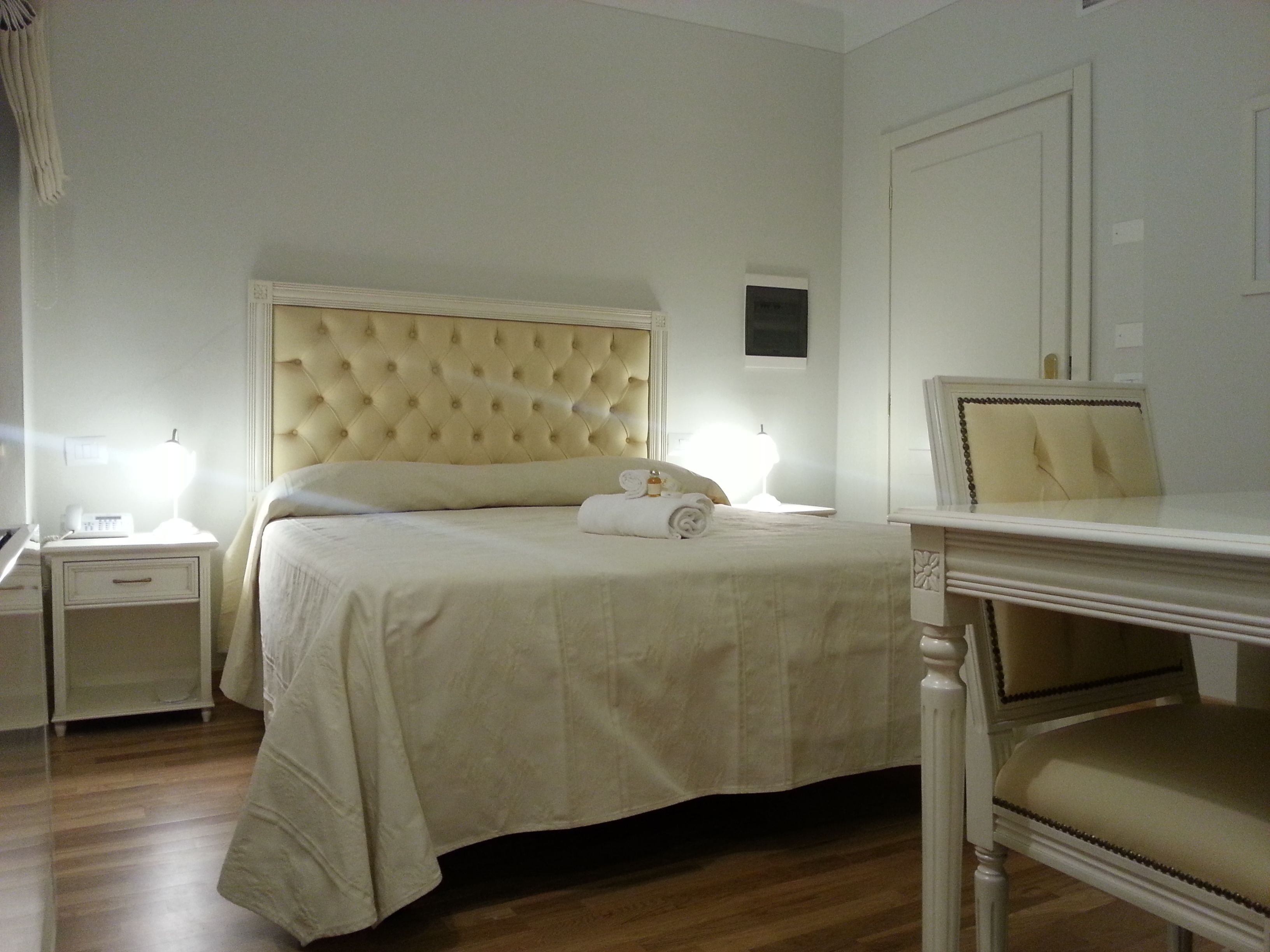 Habitación de hotel ordenada con una cama grande, mesitas de noche, una silla y un escritorio pequeño.