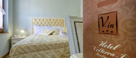 A hotel room with a large bed, a bedside table with a lamp, and a wall with a welcome sign.